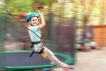 穿着头盔的可爱的小花公子金发女孩在冒险公园玩得很开心图片