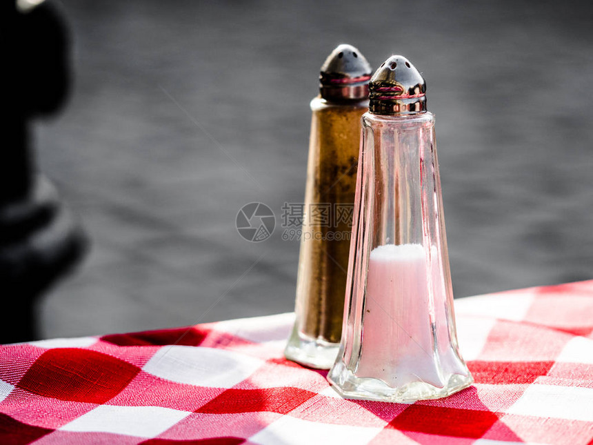 海盐片和浅色苏格兰焦油餐巾上的鲜土黑胡椒边上的两个小摇晃器图片