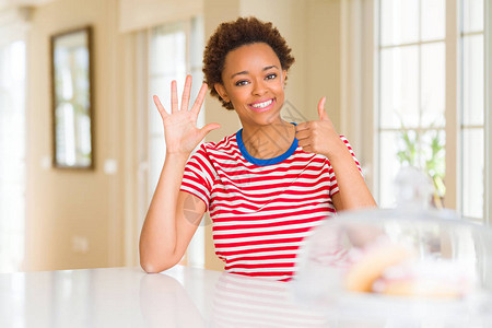 年轻美丽的非洲裔美国女人在家里展示并用六号手指向上指点图片