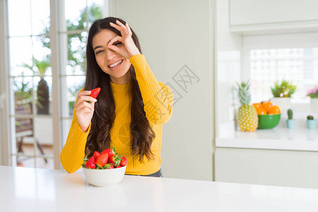 年轻女人吃新鲜红草莓作为健康的零食快乐的笑脸微笑做一个好标记用手盯着图片