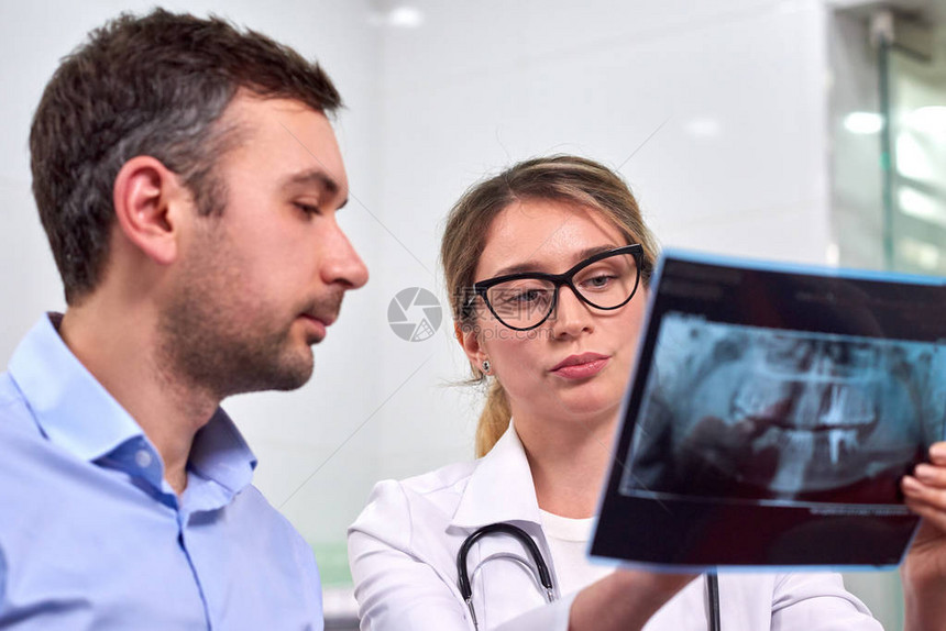 白种女牙医向男病人解释牙科柜室的图片