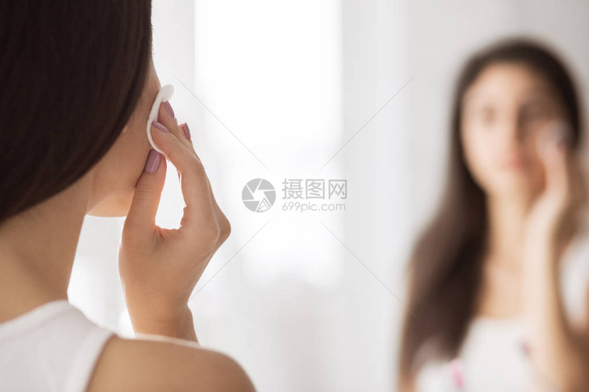 在浴室镜子前洗手间用垫子擦脸的年轻女子图片