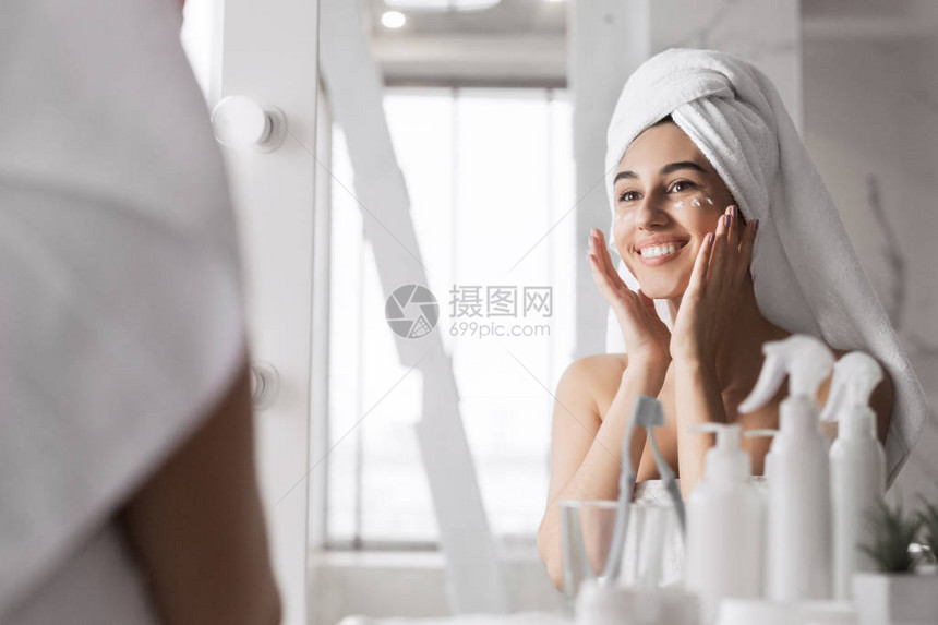美丽的年轻女子在浴室的脸上涂奶油图片