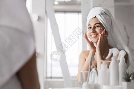 美丽的年轻女子在浴室的脸上涂奶油背景图片