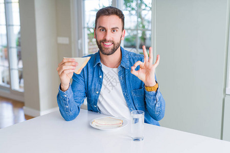 英俊男人吃健康的三明治用手指做一个好标志图片