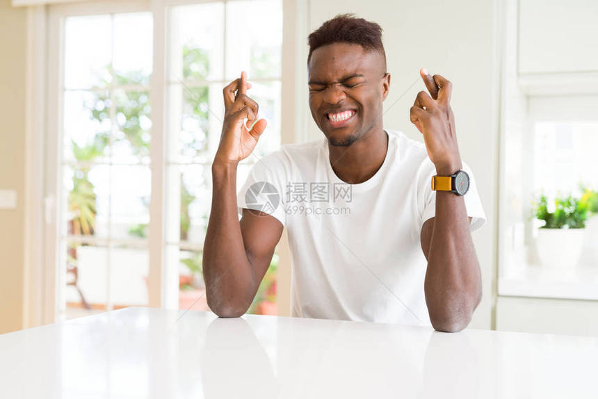 坐在白桌上的非洲帅哥在家中微笑地跨过手指图片