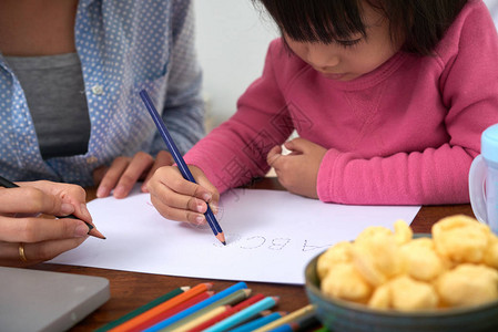 有母亲的作物小女孩在家里用彩色铅笔和学习字母图片