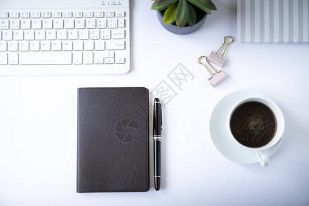 办公桌顶部视图或平面布满白色背景白键盘咖啡杯黑笔记本粉红色纸图片
