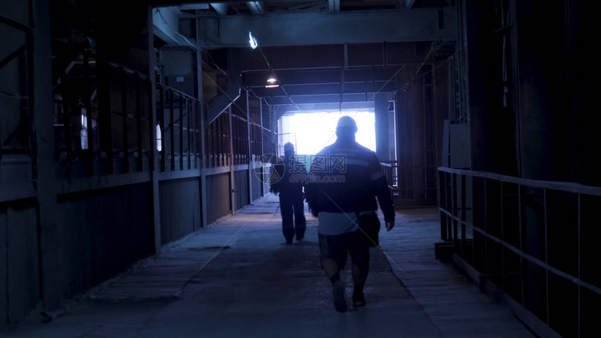 在冶金厂生产大厅上行走的产业工人剪影的后视图跟随工程师走过重工业图片