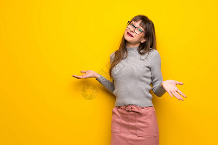 在黄色墙上戴眼镜的女人举起肩膀时做出无图片