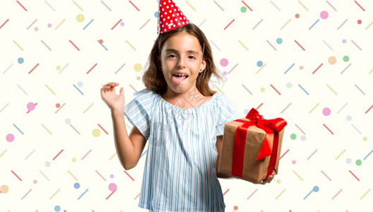 有个小女孩在生日派对上拿着礼物的小女孩在摄影机前放舌头笑图片