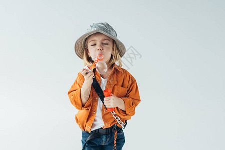 穿着帽子和橙色衬衫的可爱孩子吹着灰色隔图片
