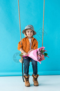 可爱的小孩坐在摇摆上拿着花束看着蓝色图片