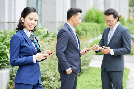 拥有智能手机户外与背景男同事一起站立的美丽优图片