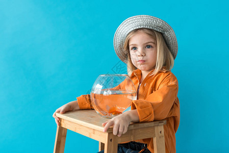 戴着银色帽子和橙色衬衫的孩子拿着有金鱼的水族箱图片