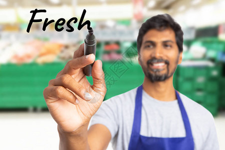 封闭或印度男子杂货店或超市雇员用黑标记在无形显示上写新文图片