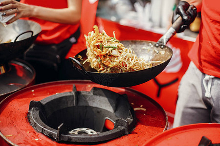 亚洲街头美食节在城市厨师在火锅里煮面条和蔬菜明火炒中式日本背景图片