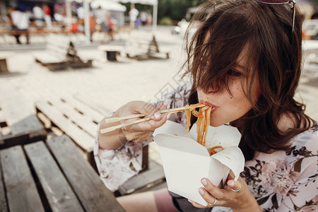 时尚的时髦女孩用竹筷子从纸箱里吃炒面配蔬菜和海鲜亚洲街头美食节波西米亚女人在纸盒背景图片