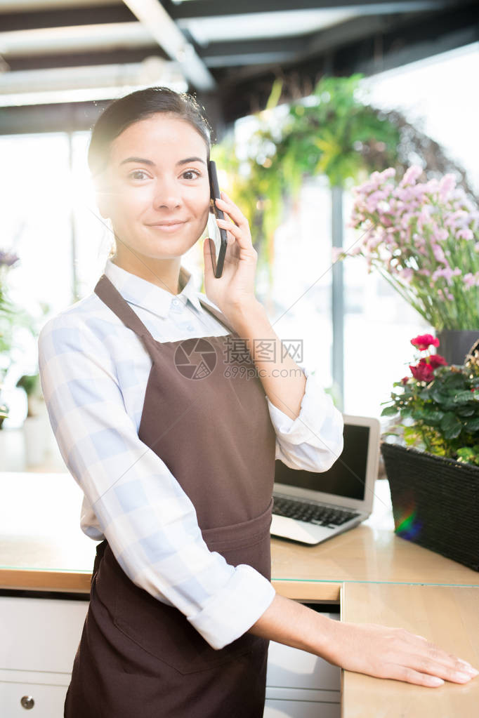 当代花店的年轻员工在用智能电话咨询客户时图片