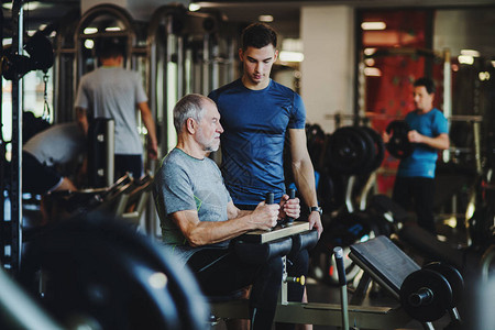 一名高级男子和一个年轻的男教练在健身房锻炼图片