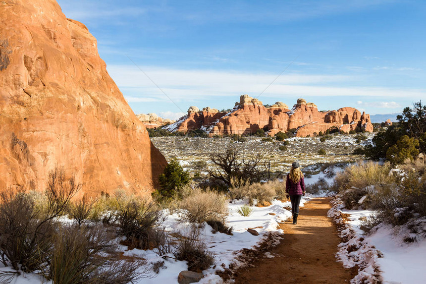 在红沙石小径上徒步的女子环绕着Arches公园里满是鲜雪和图片
