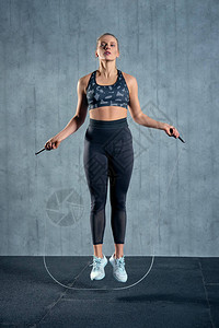 适合年轻女子跳绳在灰色背景下用跳绳锻炼肌肉的年图片