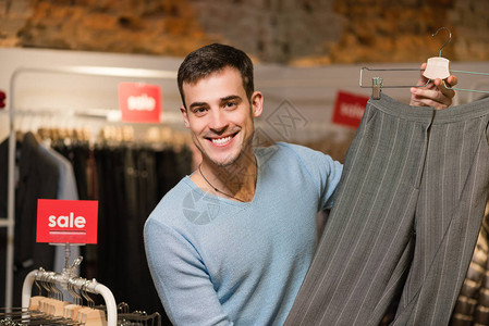 微笑与经典女裤子在店里的男销售顾问有吸引力的卖家展示在服装精品店图片