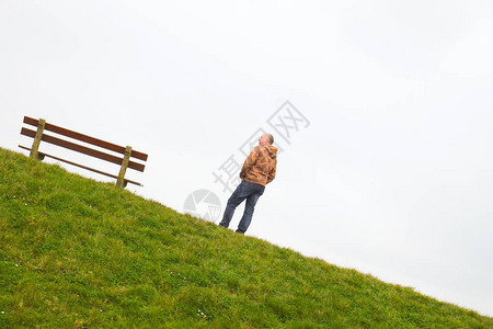 一个人站在草地上方地平线上的一张空木凳旁边图片