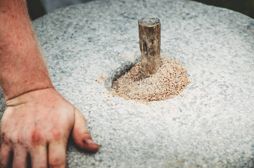 古老的quern石手磨与谷物关闭这个人在磨石的帮助下将谷物磨成面粉男士手放在磨石上用手图片