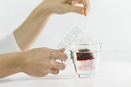 一位女手将一袋芙蓉茶浸入装满水的玻璃杯中的特写图片