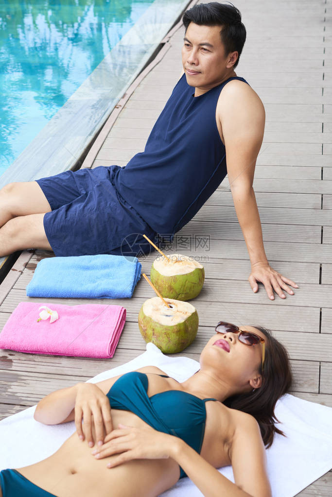 戴着墨镜的年轻美女躺在泳池边晒日光浴图片