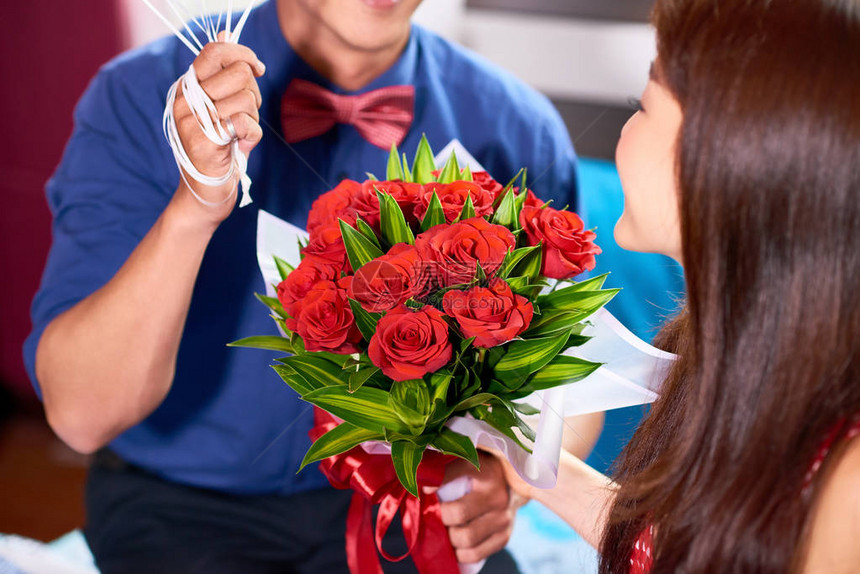 紧贴男人拿着一束漂亮的玫瑰花送给他的女朋友庆祝结婚纪念日的图片