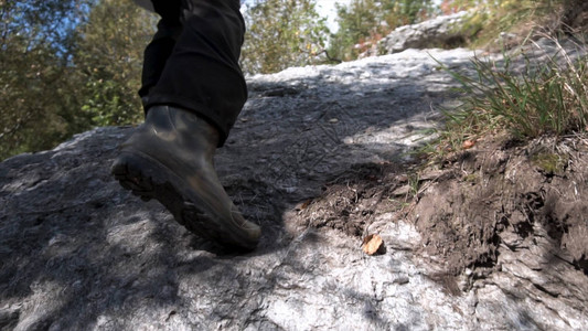 在山上的枯草丛中徒步旅行时关闭男子橡胶靴登山者的腿攀图片