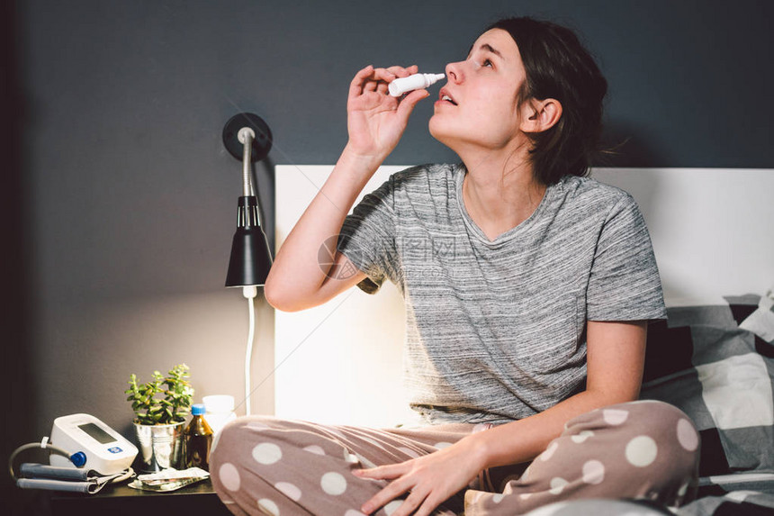 主题是季节感冒流鼻涕流感感染在家卧室床上的年轻白种女人在她的鼻子里喷药滴鼻涕过敏图片
