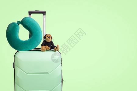 带轮子的塑料手提箱毛绒玩具旅行枕绿色背景儿童旅游理念图片
