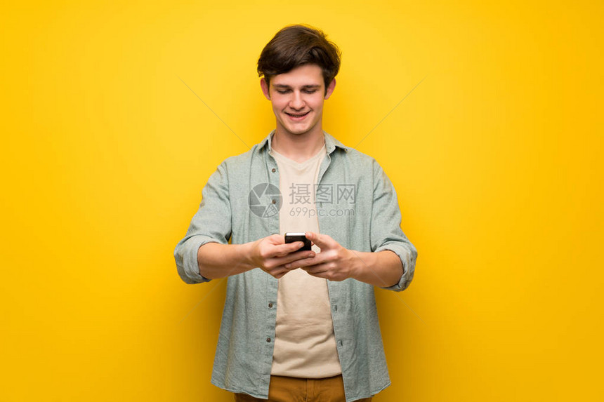 黄墙上的青少年男子用手机传递信图片