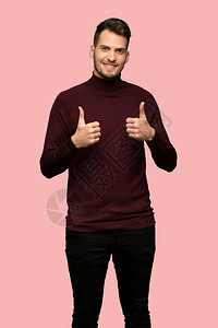 穿着上衣和大拇指的毛衣的男人因为粉红背景发生了一件好事图片