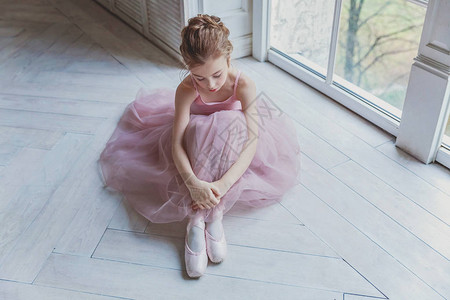踮脚尖小女孩舞蹈课上的年轻古典芭蕾舞演员女孩美丽优雅的芭蕾舞女演员在白光大厅里穿着粉色短裙背景