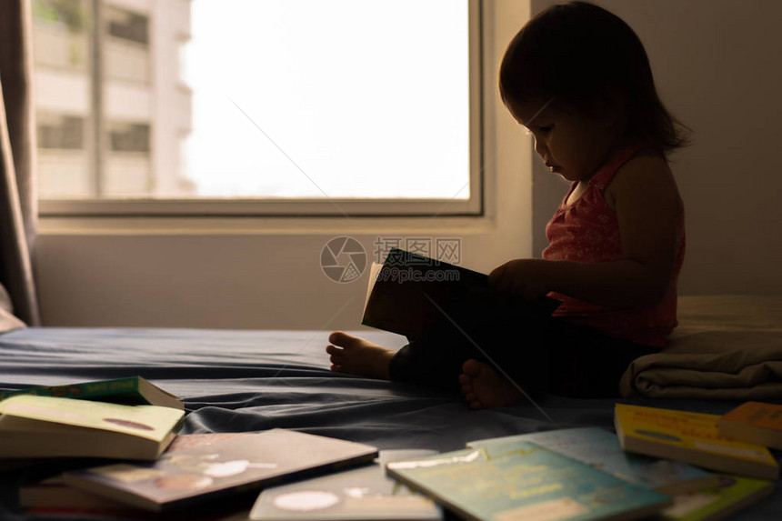 聪明的孩子在她的床上看书学习如何阅读图片