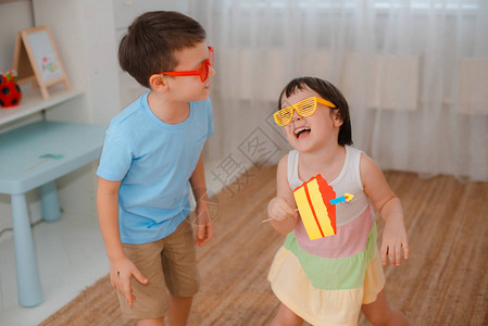 男孩和一个女孩用蜡烛玩道具纸蛋糕生日那天孩子们一起咬蛋糕的表演朋友们戴着有色眼镜玩得背景图片