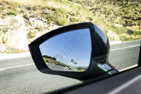 一辆停在肩膀上的汽车的镜子玻璃中反射出图片