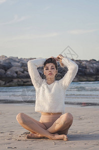 穿着白色毛衣和米色泳装的漂亮女模特坐在靠近海洋或大海的滩上图片