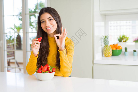 年轻女人吃新鲜红草莓作为健康的零食用手指做好记号图片
