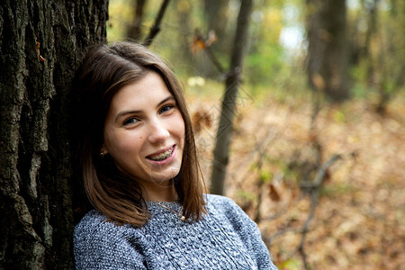 长着牙套的年轻美女穿着灰色毛衣坐在秋天的森林里图片