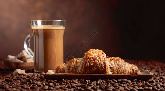 咖啡拿铁和羊角面包放在有咖啡豆的桌子图片