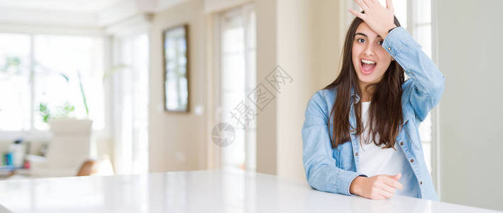 美丽的年轻女子坐在家里的白桌子上的广角图片惊讶地用手在头上犯错图片