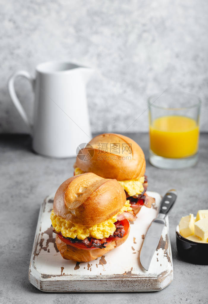 早餐三明治配炒鸡蛋培根奶酪白木板上的番茄新鲜橙汁的玻璃白色背景制作早餐概念图片