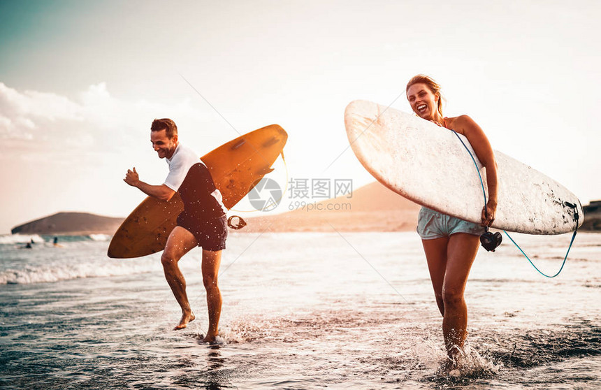快乐的冲浪夫妇在海边用冲浪板跑步型人在日落时一起玩冲浪极限冲浪和青年关系图片
