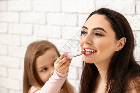 可爱的小女儿用唇膏在母亲嘴唇上涂白砖图片