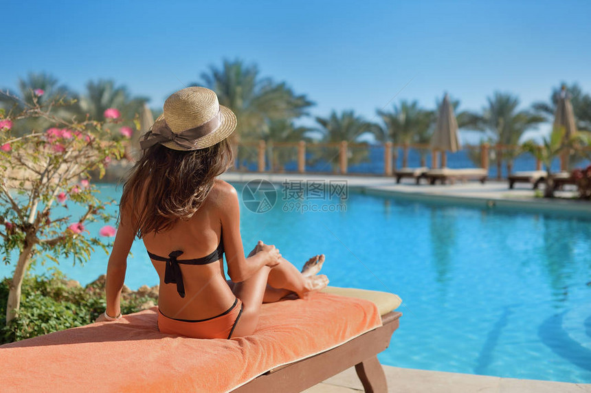 在埃及豪华的夏日泳池酒店附近的白日床上放松穿着稻草帽的女人概念图片